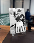 Black and white image of a man in a suit and hat holding a paper. Vintage decor on a desk.