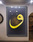Decorative wall art featuring a bold yellow Arabic letter on a dark background, illuminated by recessed lights.