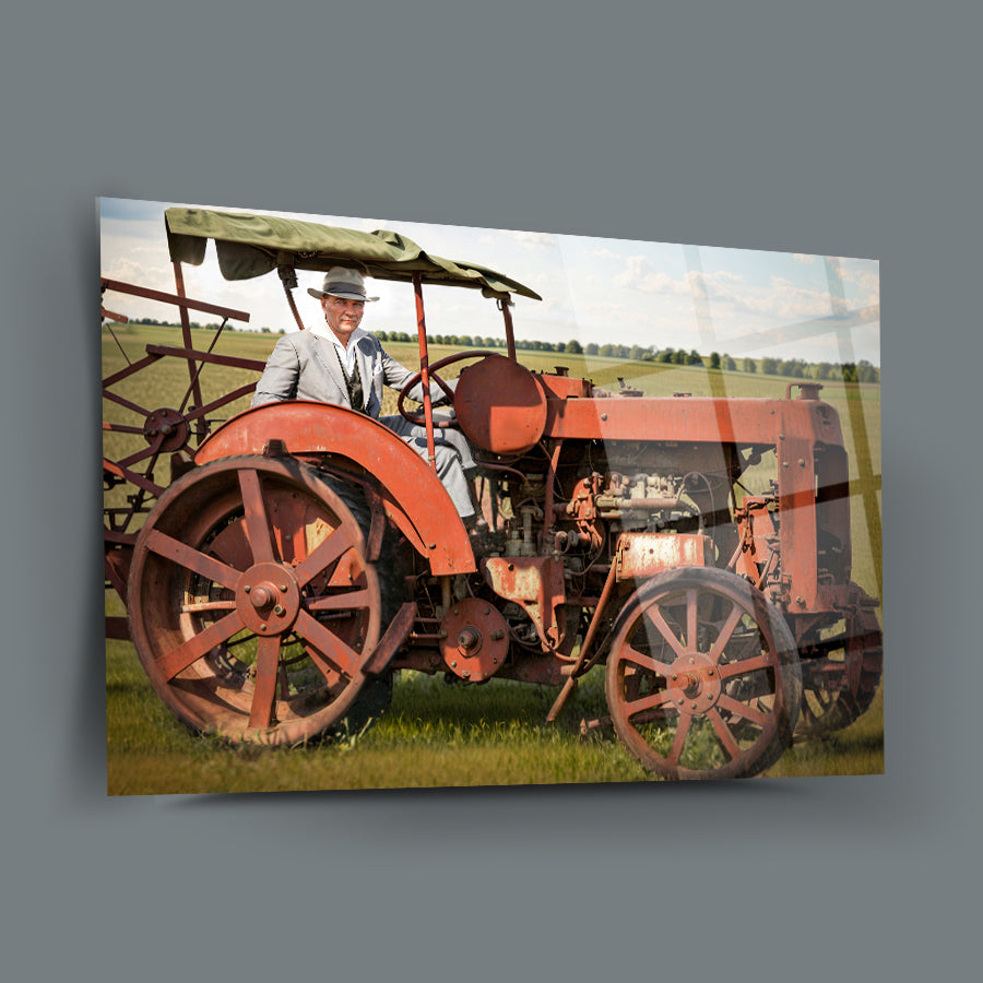 Historical image of a man in a suit on a vintage red tractor in a green field.