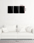 Modern 3-piece black glass art set above a white sofa, dimensions labeled for each panel.
