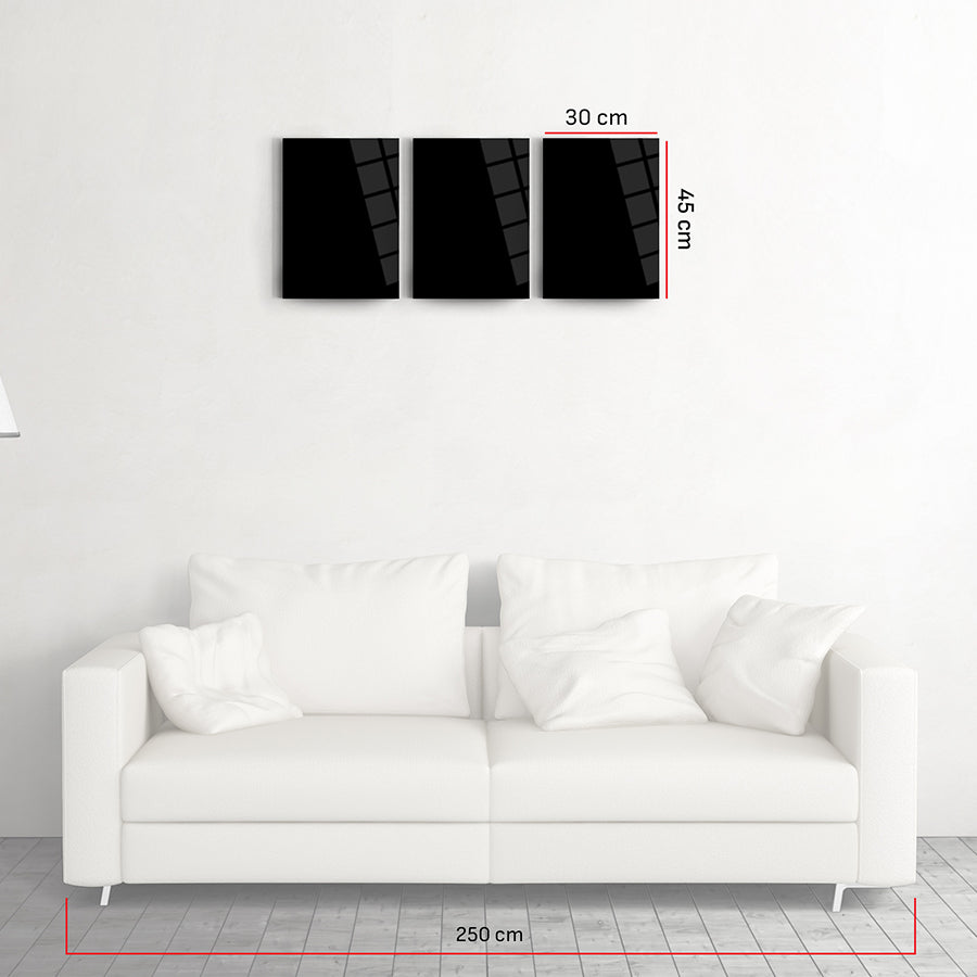 Three-piece black glass wall art set above a white sofa, enhancing contemporary home decor with modern design.