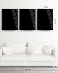 A set of three black framed glass artworks above a white modern sofa in a stylish interior setting.