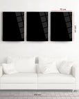Set of three black tempered glass wall art pieces above a white sofa, measuring 70 cm each.