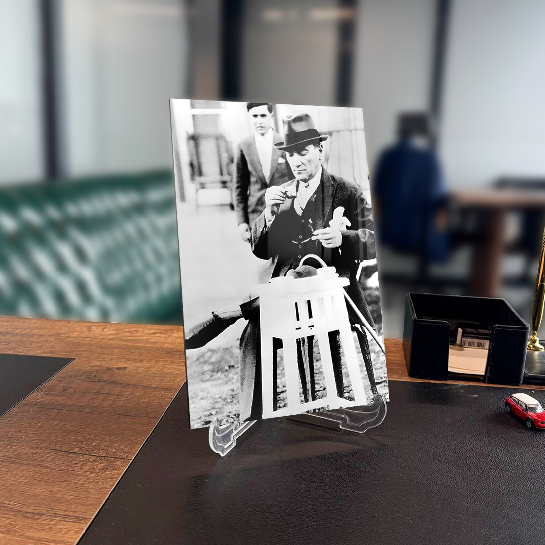 Black and white image of a man in a suit and hat holding a paper. Vintage decor on a desk.